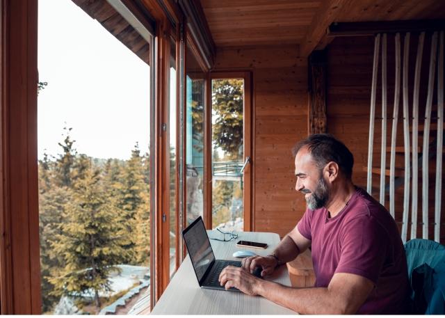 Man working remotely from a balcony overlooking a lush landscape of trees