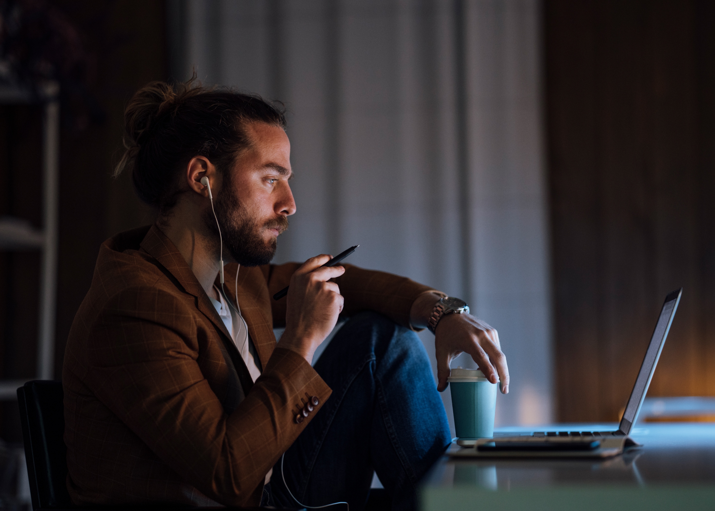 Man with pen in hand, looking at laptop