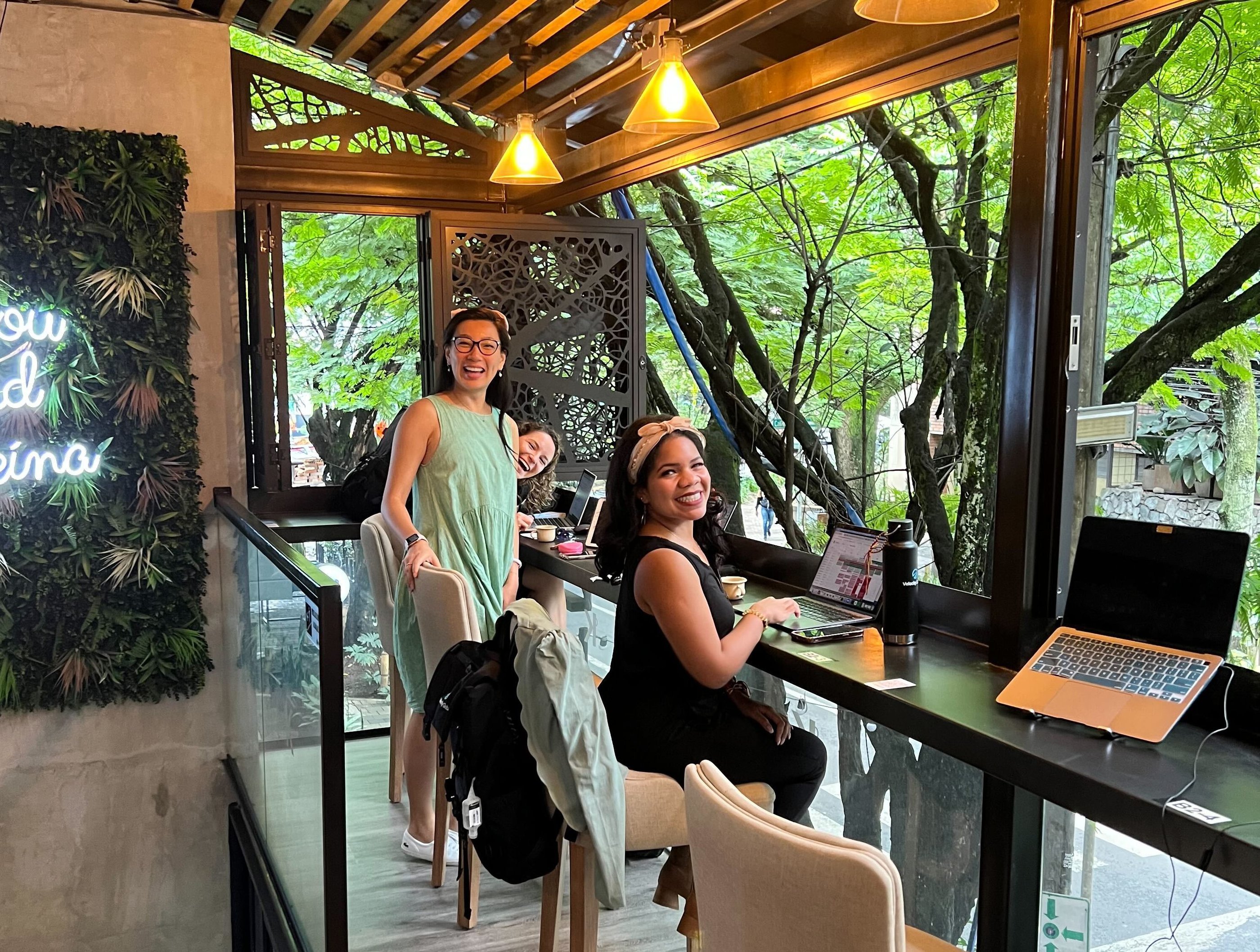 Two woman at a co-working office, hanging out by a bar like table, overlooking green vegetation