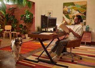 Man in his apartment working at a desk with a dog walking by