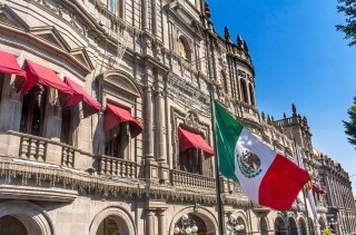 Mexican flag flying in front of buildings on the streets of Puebla, Mexico.