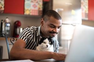 Man with a cat in his lap working on his computer