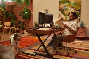Man in his apartment working at a desk with a dog walking by
