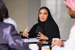 Saudi Arabian woman wearing a hijab speaks with co-workers around a conference room table