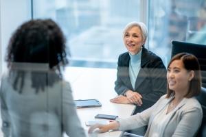 Three female HR professionals discuss work-related matters while gathered around an office conference room table