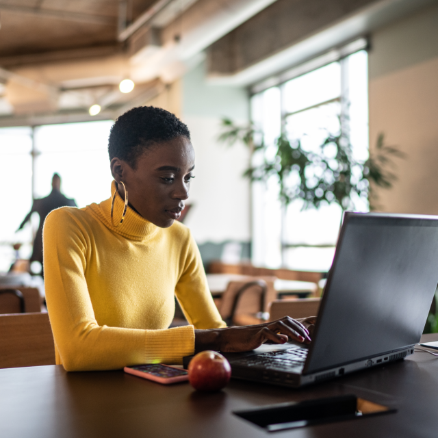 woman in yellow sweater sitting at a laptop in a public space