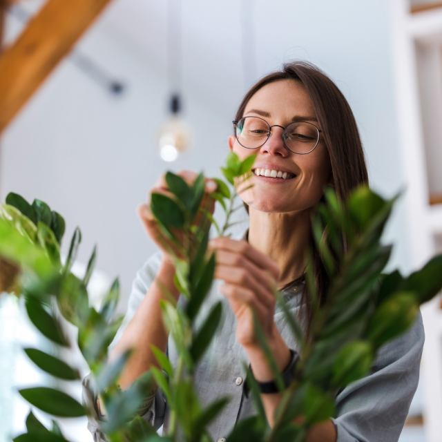 Woman with glasses smiles while tending to a plant