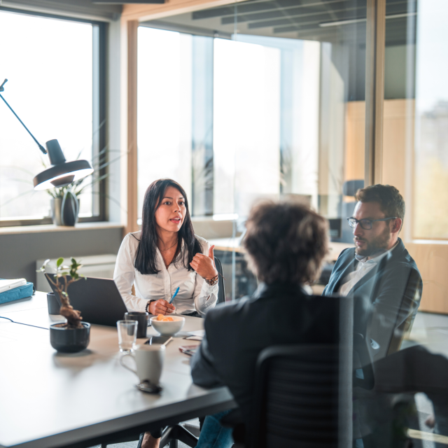 three people sitting at conference table talking