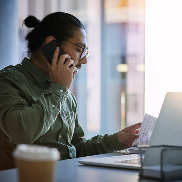 Man talking on the phone while looking at papers on his desk