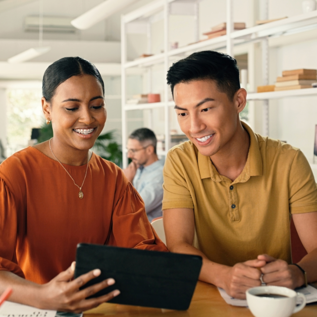 Man and woman at a coffee shop smiling, while looking at an iPad