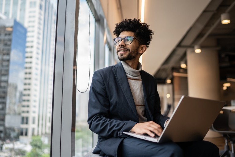 Employee sitting on window sill with laptop at office