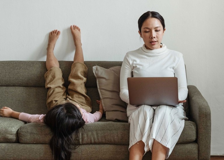 Woman on couch working on her laptop next to her young child
