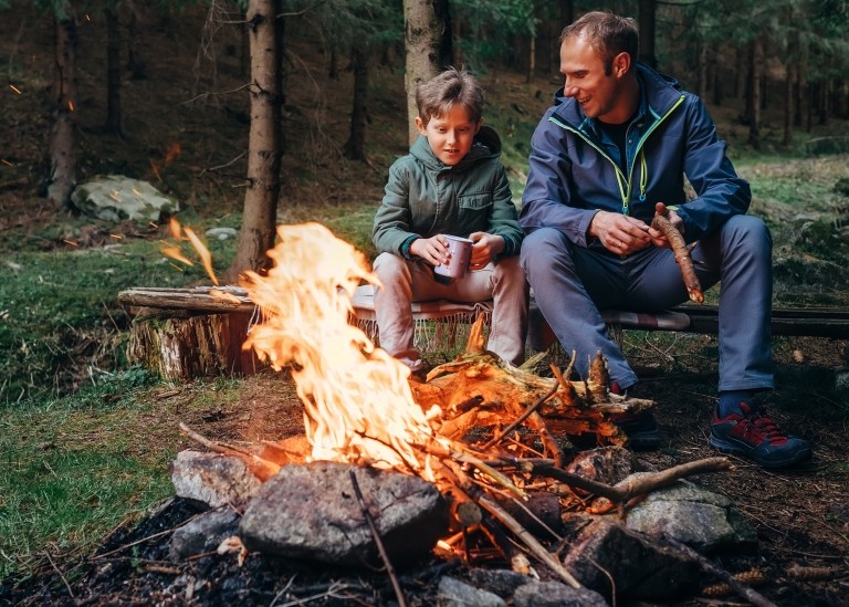 Father and son sitting by the fire at camping site. 