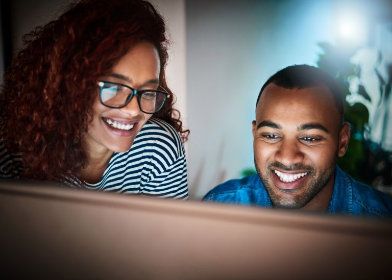 Man and woman happily working together on a work-related project from a computer