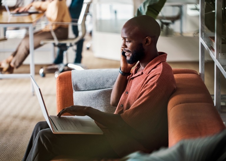 Male employee taking call on couch while on laptop