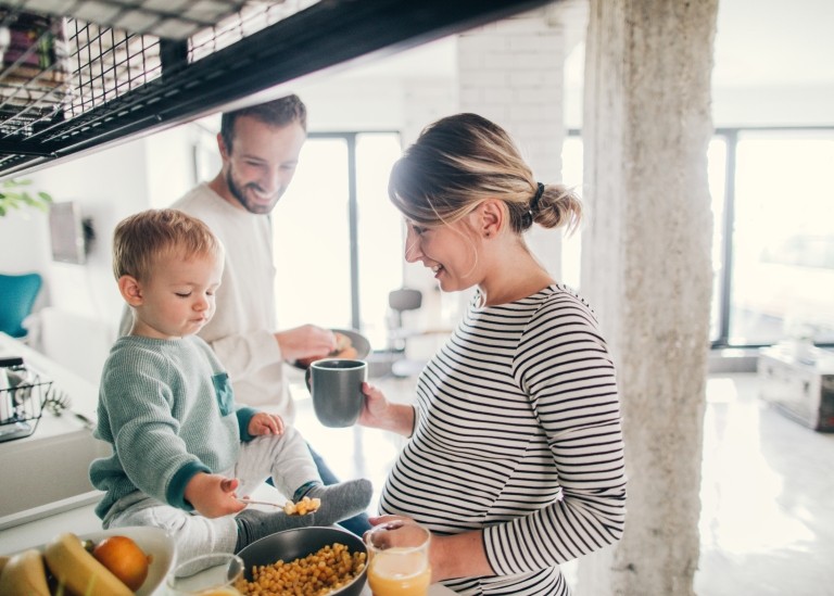 A young pregnant woman, young boy, and young man making food together in a home kitchen