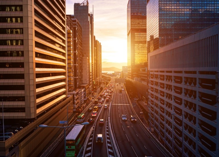 Traffic in downtown city interstate with large skyscrapers on either side at dusk.