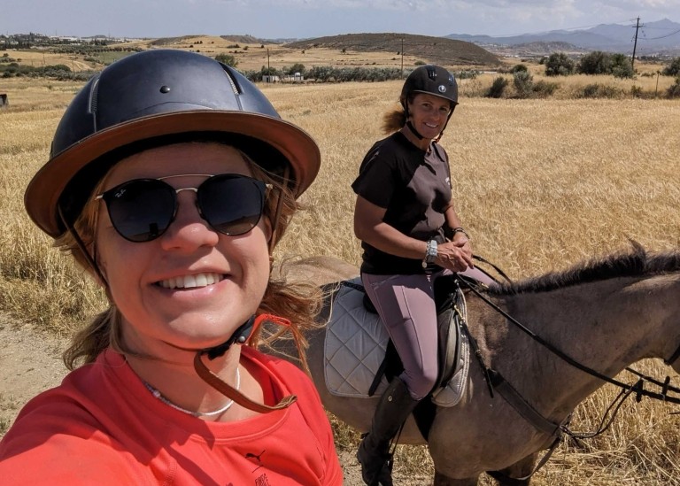 Velocity Global’s Janna Papageorghiou riding a horse with a friend while wearing a helmet and sunglasses