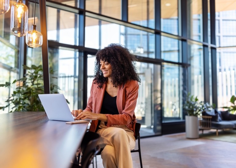 Remote employee sitting a large table and typing on her laptop enthusiastically  