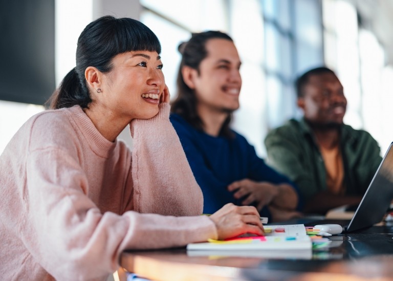 Three diverse working professionals sitting at a conference table happily engaging in work-related activities