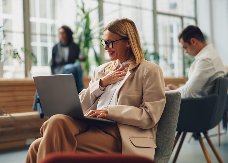 A smiling female professional performing work on her laptop in a co-working space.