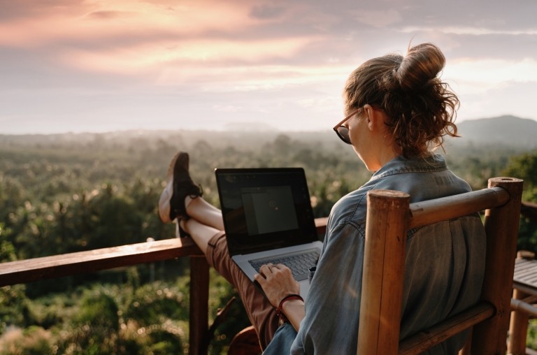 Woman working remotely from a balcony overlooking a lush landscape of trees
