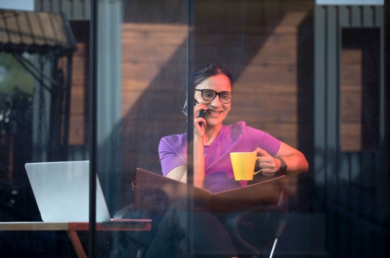 A remote employee in India engages in a work call on her mobile phone while working in a public coffee shop