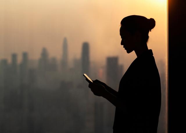 Silhouette of person on their phone. Buildings in the background.