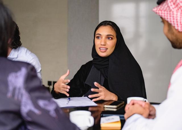 Saudi Arabian woman wearing a hijab speaks with co-workers around a conference room table